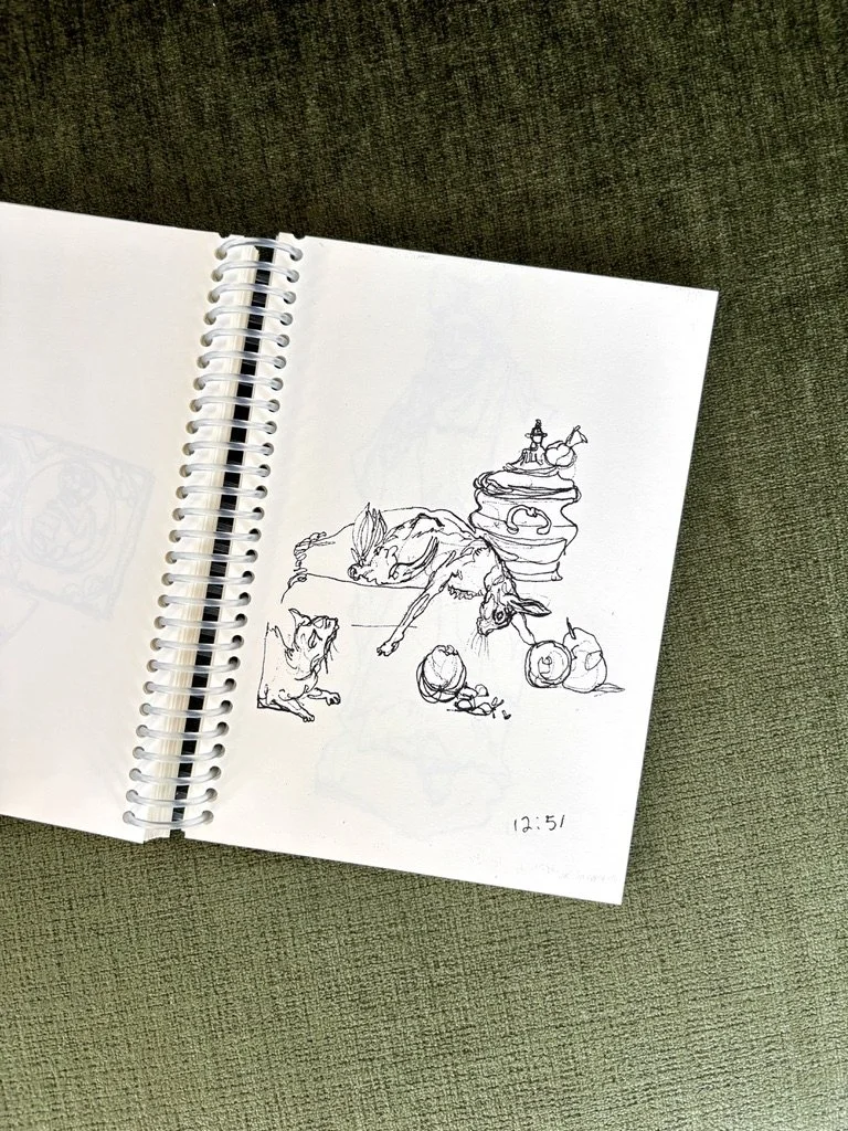 Photo of an off-white coloring book laying open at a slight angle on a plush sap-green surface. Page right includes a black ink contour line drawing of a still life with dead (hare and chicken) and living (cat) animals amongst fruits and tableware.