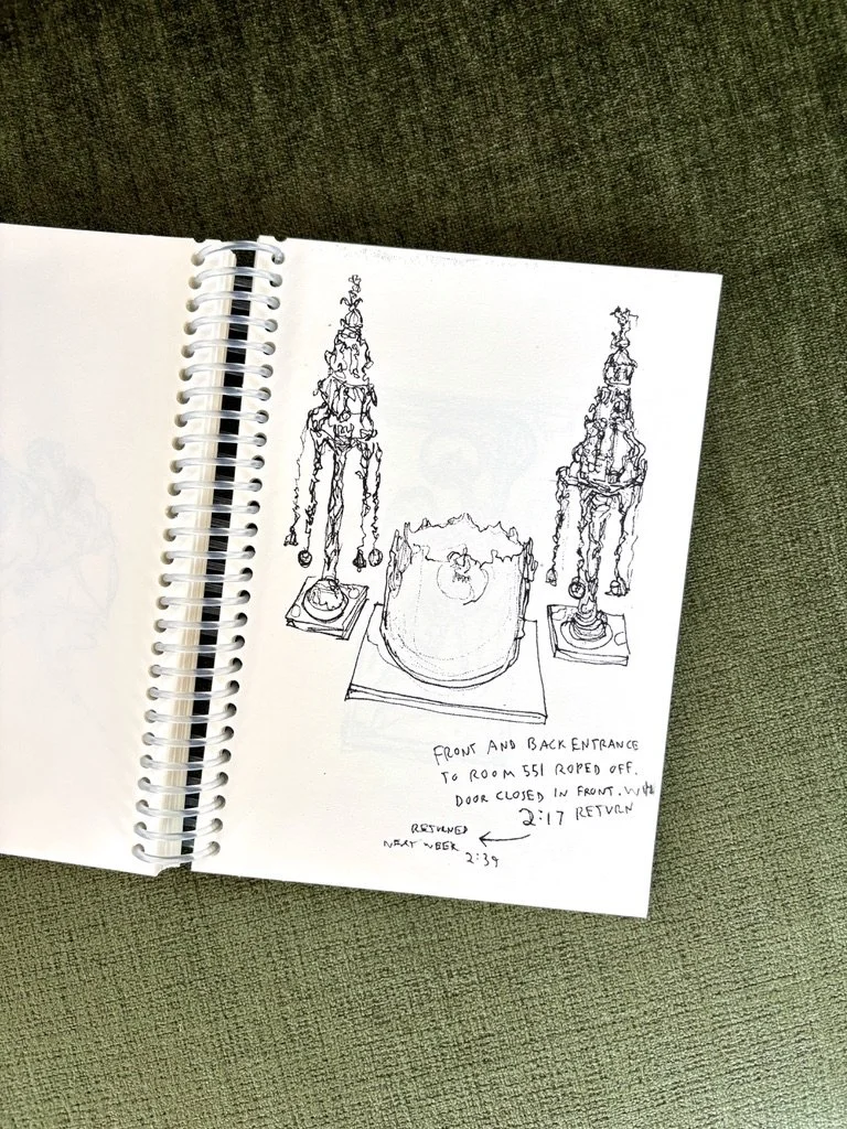 Photo of an off-white coloring book laying open at a slight angle on a plush sap-green surface. Page right includes a black ink contour line drawing of two Torah finials on either side of a Torah crown.