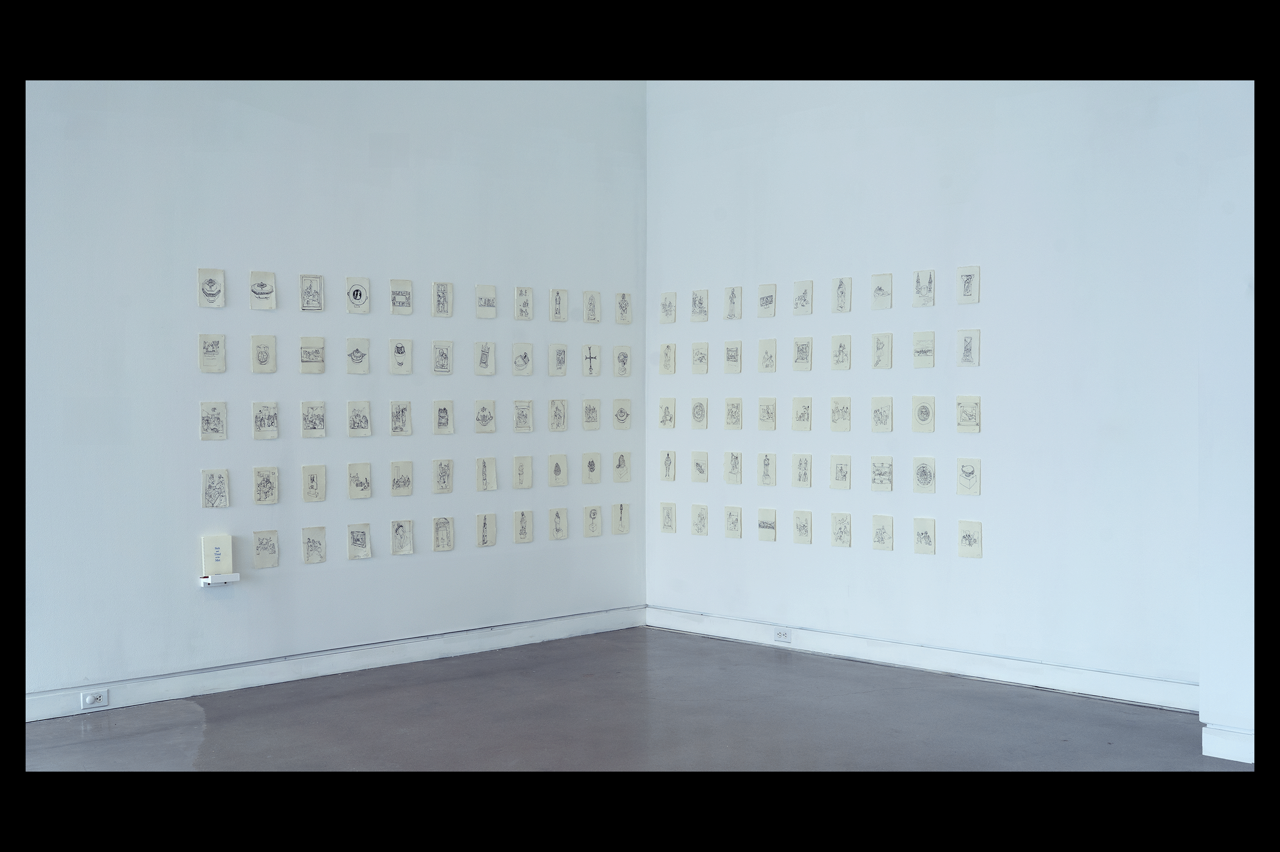 Wide-angle install photo of ninety-nine five by seven inch inch ink drawings of different museum object at the Metropolitan Art Museum drawn on handmade paper, along with one coloring book containing copies of each. Hung in a five row, twenty column grid at the corner of the white-walled, concrete floor gallery. The book sits on a small white ledge in the bottom left of the grid, accompanied by one red, yellow and blue colored pencils.